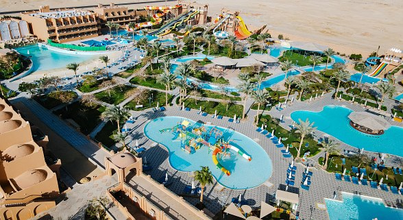 Wasserpark mit bunter Rutschenanlage vor einem burgähnlichen Gebäude, mehrere Rutschen münden in ein großes Schwimmbecken.