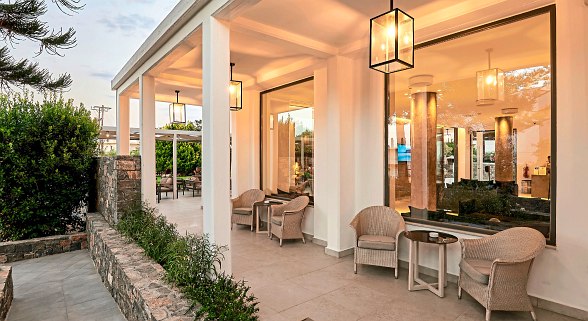Terrassenbereich mit Stühlen und Tischen, große Fenster, warmes Licht, weiße Wände, abendliche Stimmung.