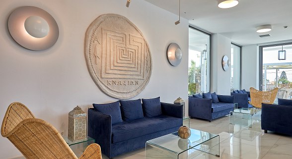 Moderner Lounge-Bereich mit blauen Sofas, Rattanstühlen, Glas-Tischen, großen Fenstern und Wanddeko in weißer Umgebung.