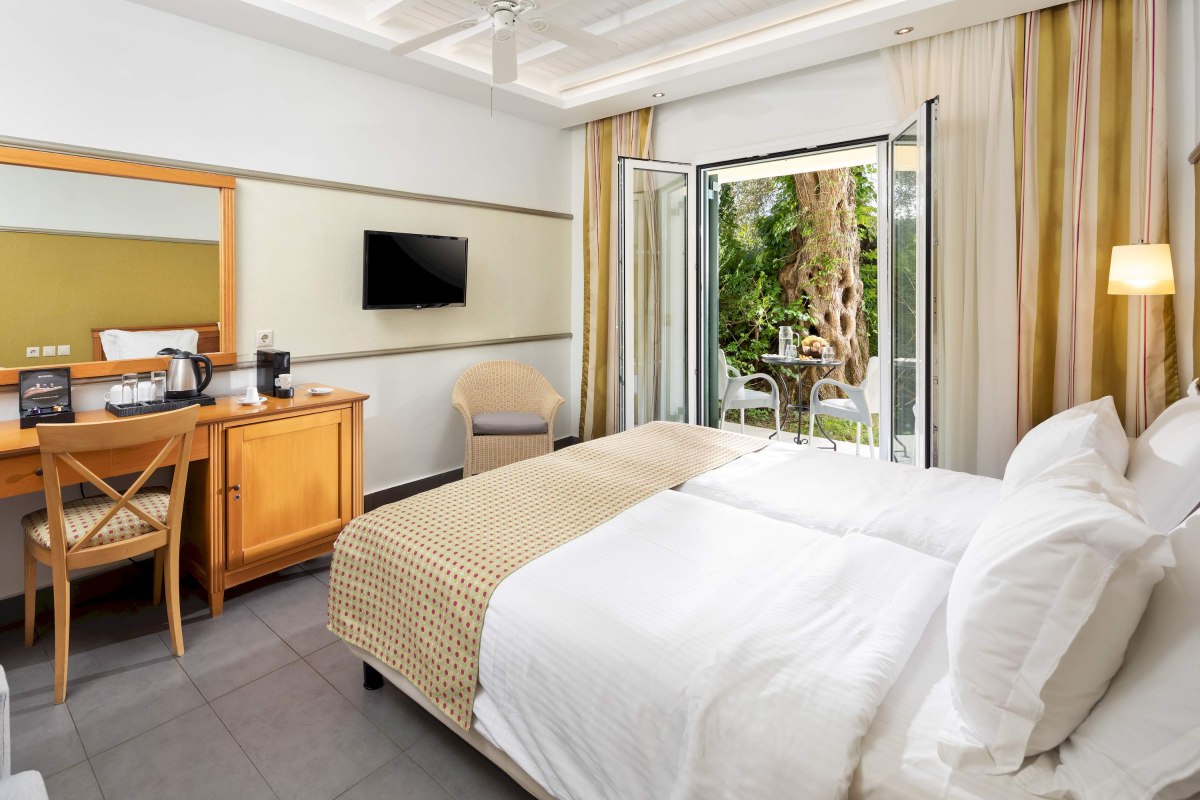 Helles Hotelzimmer mit Doppelbett, Schreibtisch, TV und Zugang zur Terrasse mit Gartenblick.