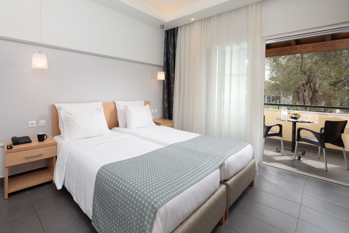 Helles Zimmer mit Twinbett, Nachttischen und offenem Fenster zum möbliertem Balkon.