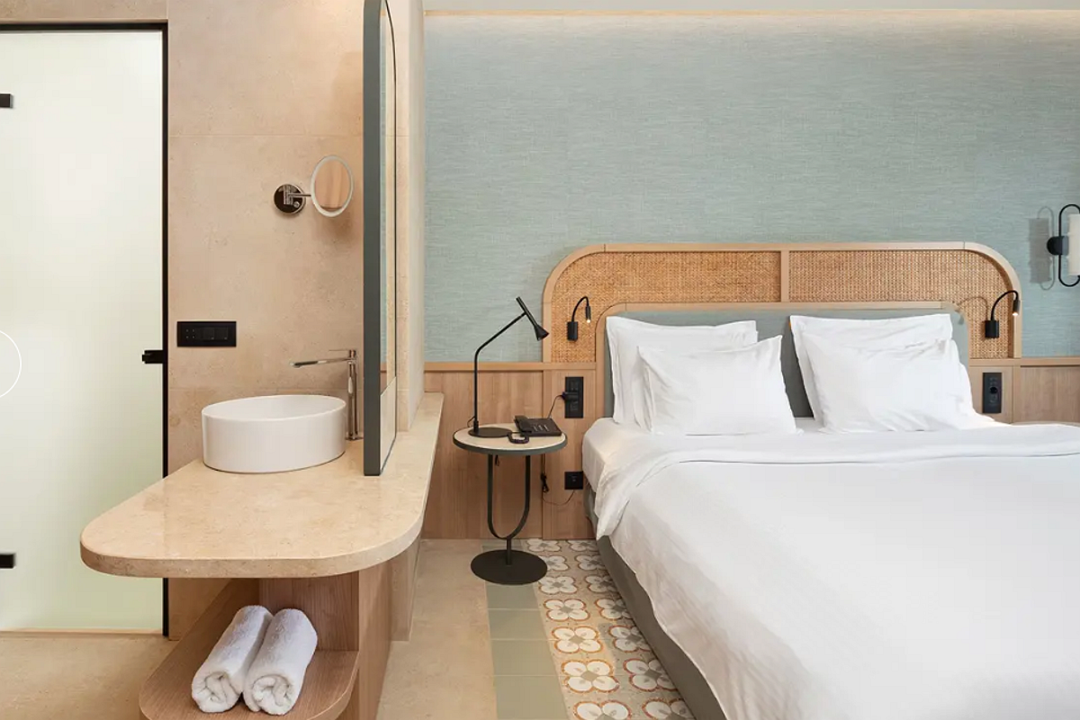 „Modernes Hotelzimmer mit Doppelbett, offenen Türen zum Bad und Ankleidebereich in warmen Holztönen.“