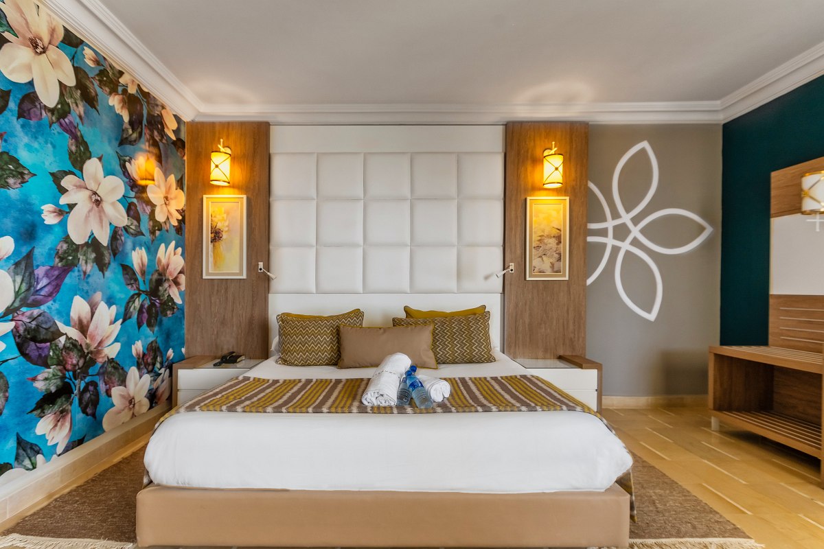 Modernes Hotelzimmer mit Doppelbett, großen Kleiderschränken, Sitzbereich und auffälliger Blumenwand.