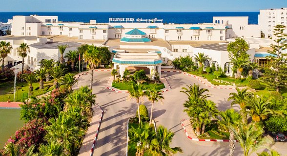 Luftaufnahme eines großen Strandhotels mit Poolanlage, Sonnenschirmen, Liegen und direktem Zugang zum Sandstrand.