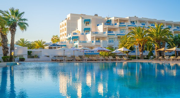 Luftaufnahme eines großen Strandhotels mit Poolanlage, Sonnenschirmen, Liegen und direktem Zugang zum Sandstrand.