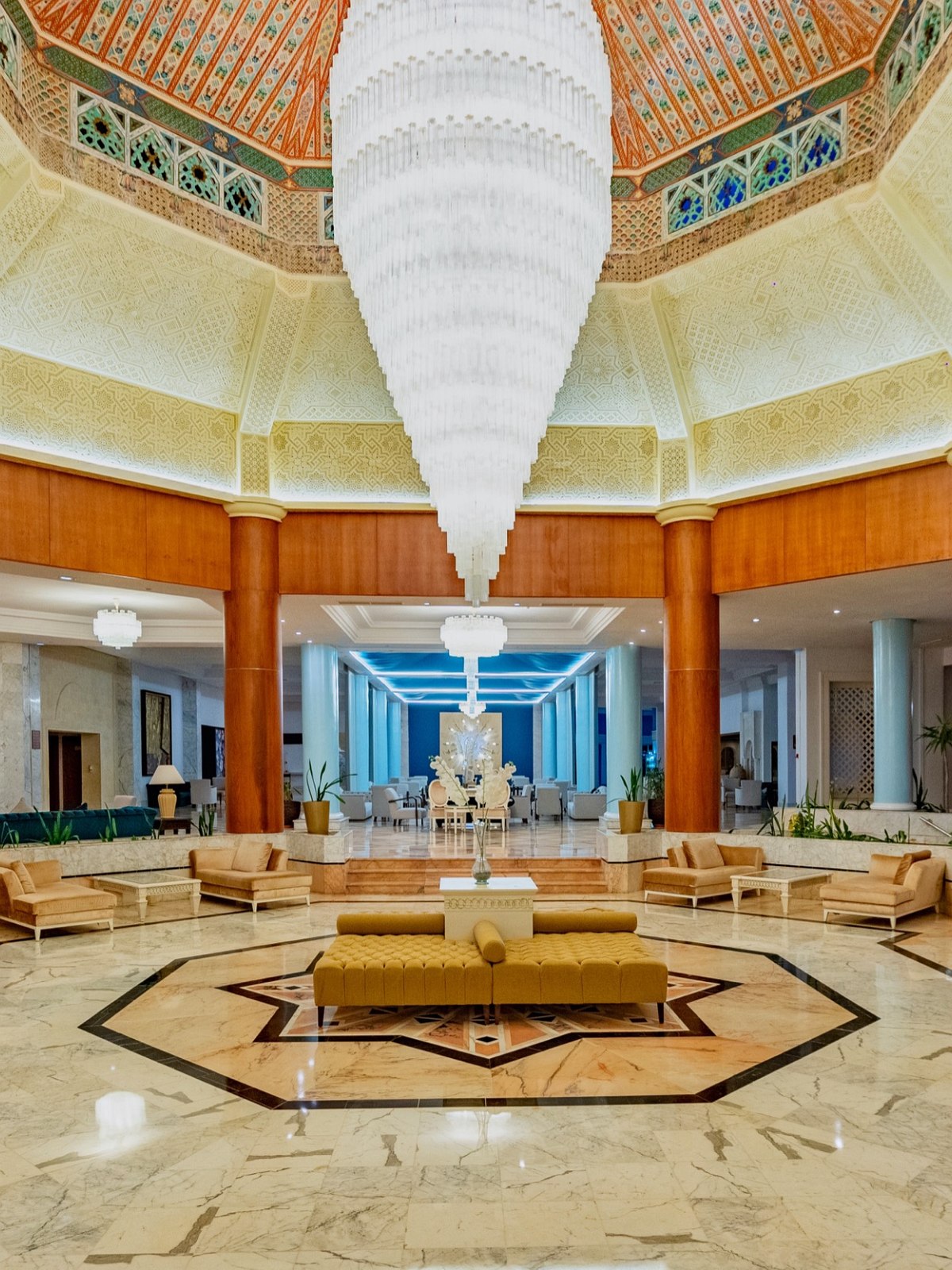 Elegante Hotel-Lobby mit türkisfarbenem Deckenakzent, luxuriösen Sesseln und Marmorboden in warmer Beleuchtung.