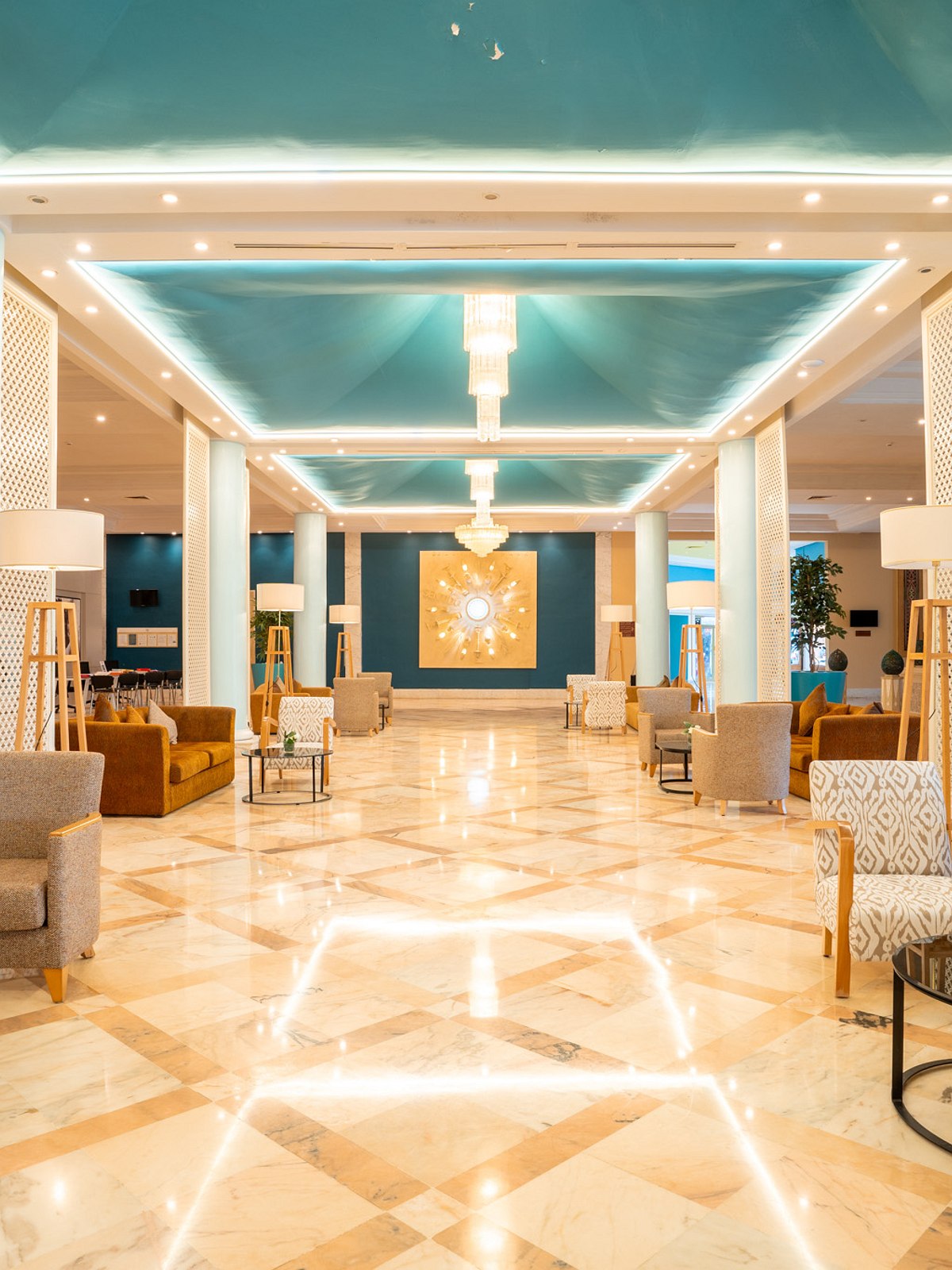 Elegante Hotel-Lobby mit türkisfarbenem Deckenakzent, luxuriösen Sesseln und Marmorboden in warmer Beleuchtung.