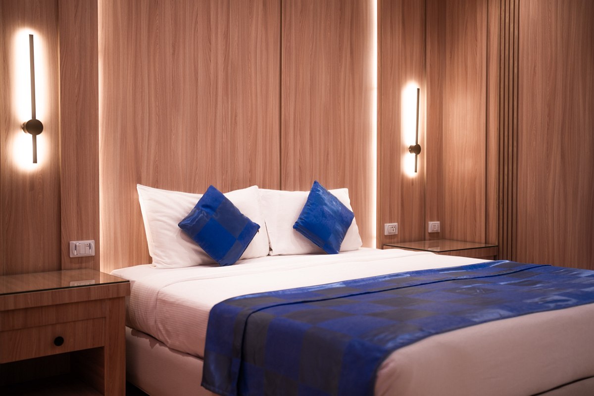 Helles Hotelzimmer mit Doppelbett, Sofa, Schreibtisch und Balkon, warme Beleuchtung und Blick ins Grüne durch große Tür.