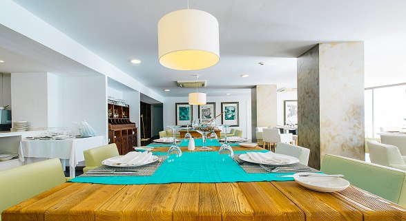 Modernes Restaurant mit gedecktem Holztisch, türkisfarbenem Läufer, eleganten Lampen und gemütlicher Atmosphäre.