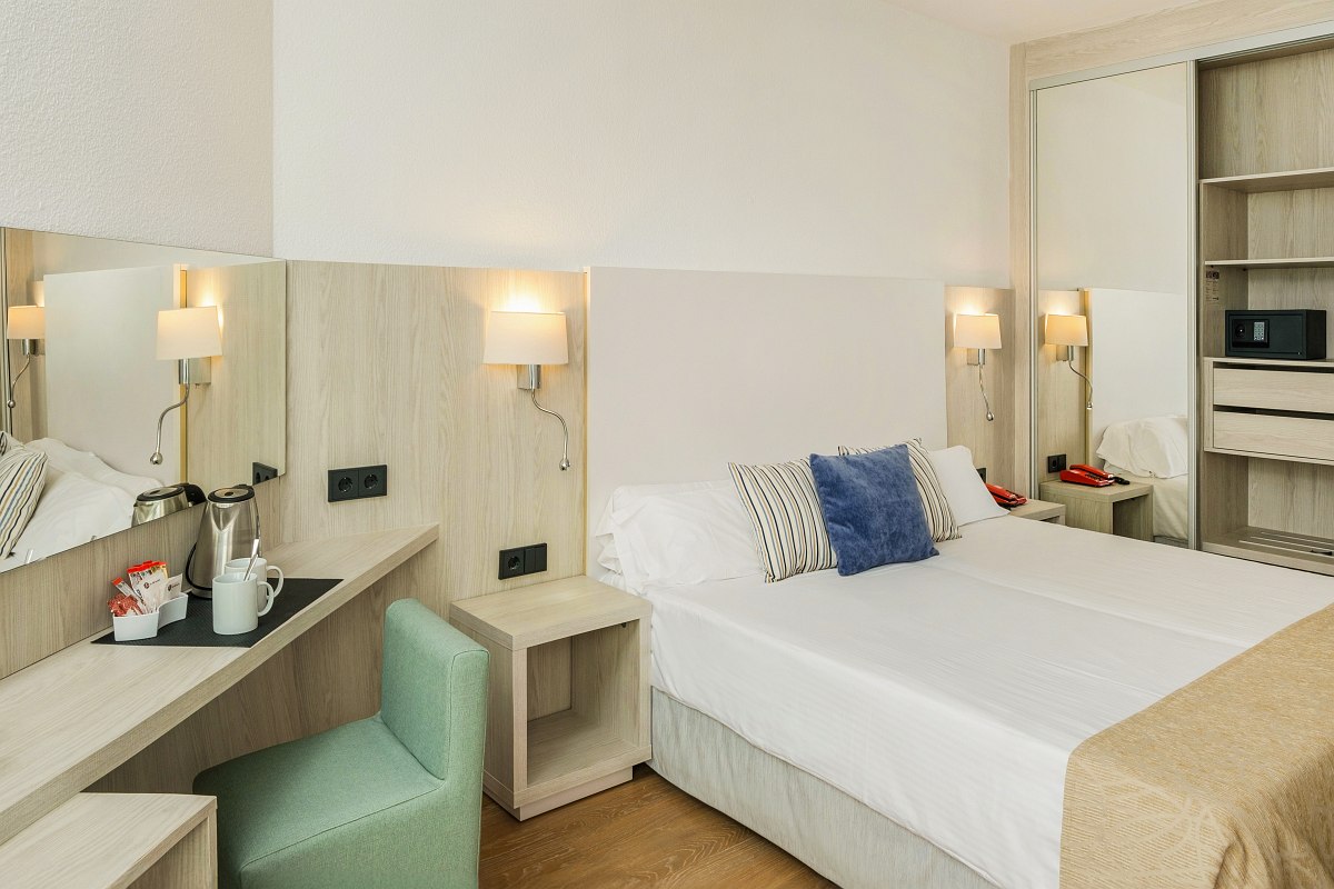 Helles Hotelzimmer mit Doppelbett, Schreibtisch, TV, Balkon mit Gartenblick und minimalistischer Einrichtung.