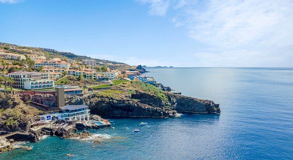 Hotelanlage auf Felsküste mit Blick auf das weite, ruhige Meer und umliegende Hügellandschaft auf Madeira.