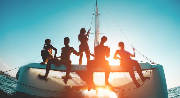 Gruppe junger Menschen entspannt und feiert bei Sonnenuntergang auf einem Katamaran auf dem Meer.