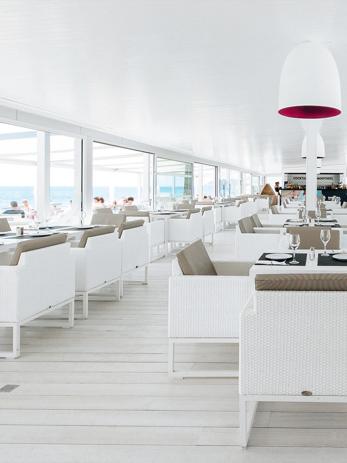 Modernes, helles Restaurant mit Meerblick, weißen Möbeln und stilvoll gedeckten Tischen in entspannter Atmosphäre.
