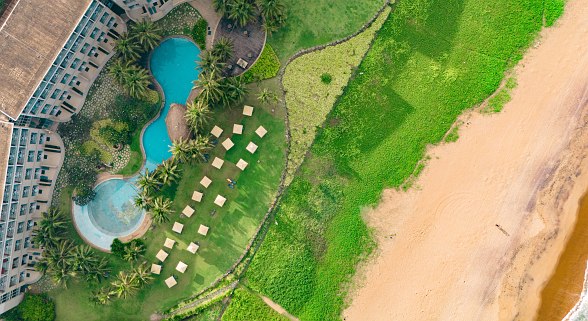 Drohnenaufnahme des Hotels Sentido Heritance Negombo mit Pools, Sonnenliegen auf Rasenfläche und direktem Zugang zum weitläufigen Sandstrand und Meer.