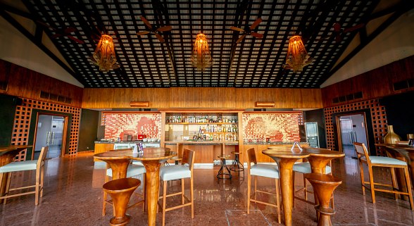 Stilvolles Hotelrestaurant mit Holzmöbeln, warmem Licht, dekorativer Decke und umfangreichem Getränkeangebot im Hintergrund.