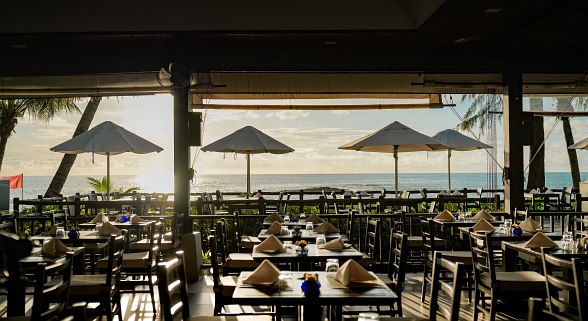  Terrassen-Restaurant im Hotel Sentido Khao Lak mit gedeckten Tischen, Sonnenschirmen und Meerblick bei Sonnenuntergang.