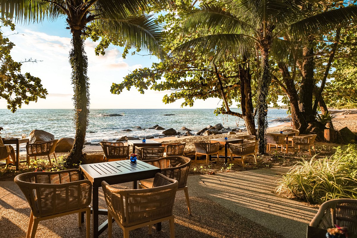 Hotel complex with two blue pools, palm trees and sun loungers, surrounded by greenery and white parasols.