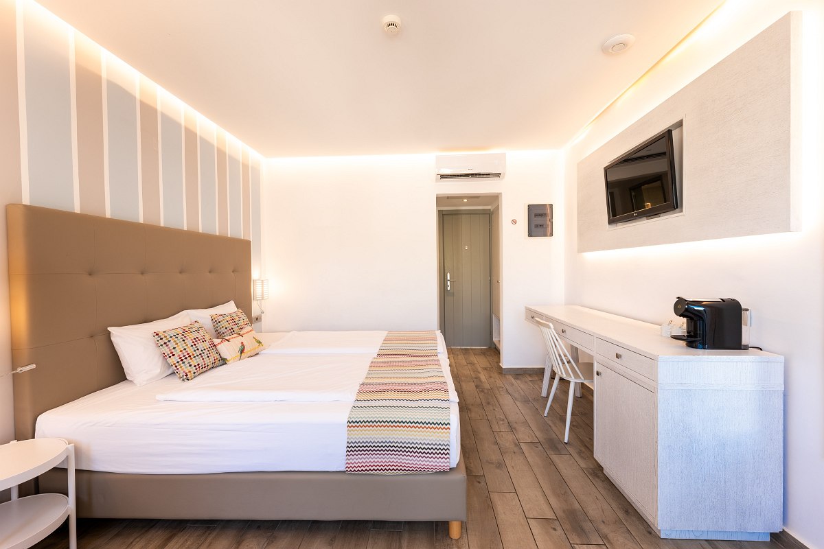 Modernes, helles Hotelzimmer mit Doppelbett, TV, Schreibtisch, Kaffeemaschine und Holzboden.