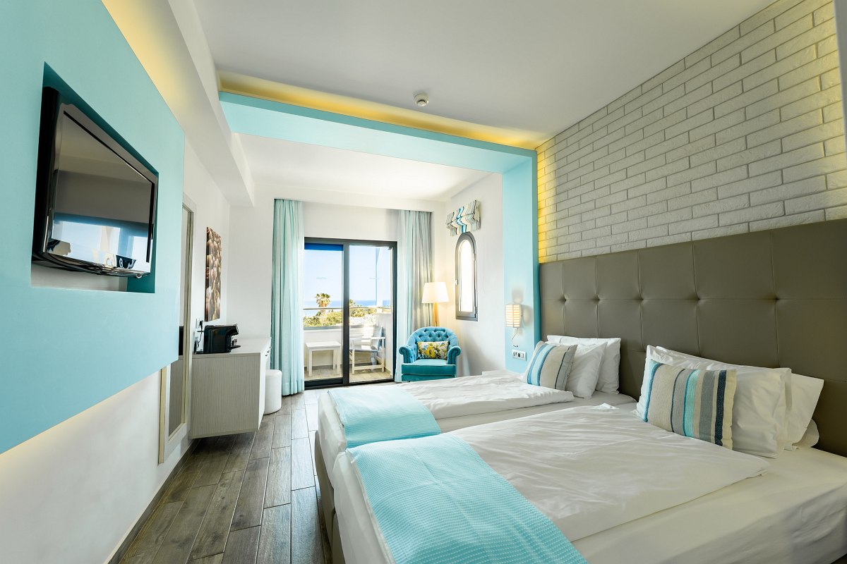 Helles Hotelzimmer mit zwei Einzelbetten, türkisen Akzenten, Balkon und Meerblick im Hintergrund.