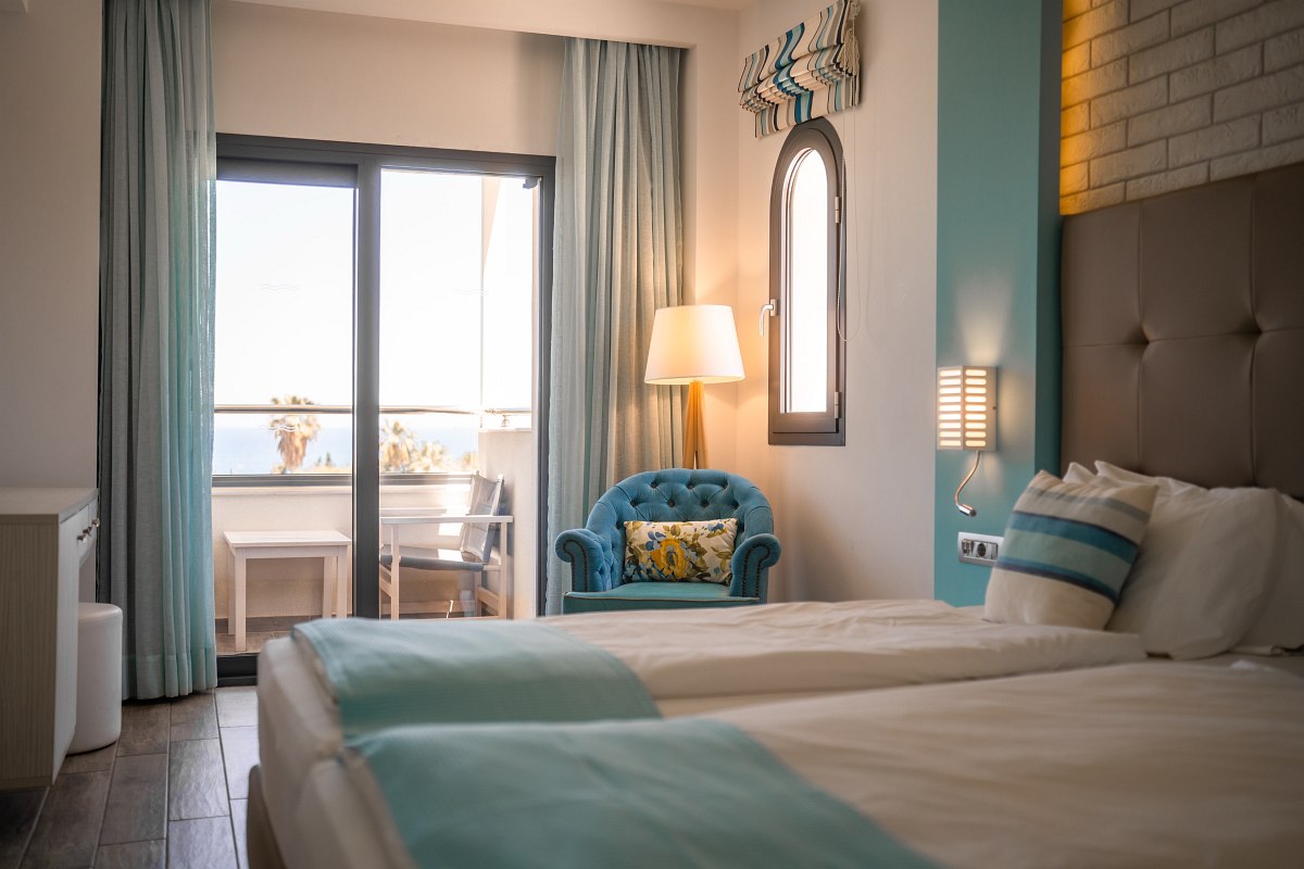 Helles Hotelzimmer mit zwei Einzelbetten, Sessel und Balkon mit Meerblick, moderne, freundliche Einrichtung in Türkistönen.