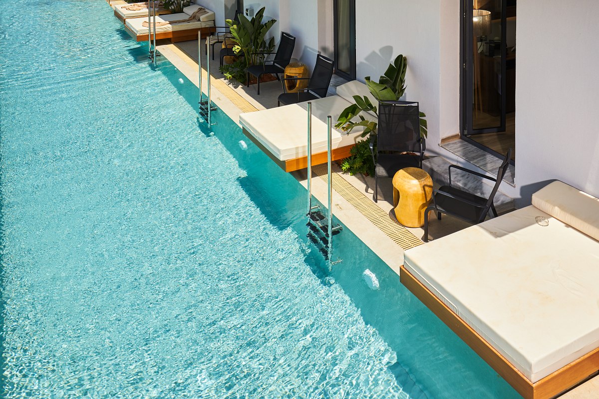 Helles Hotelzimmer mit direktem Zugang zum privaten Pool, Liegen, tropischen Pflanzen und moderner Einrichtung.