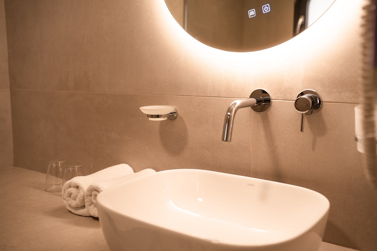 Modernes Badezimmer mit großer begehbarer Regendusche, beleuchtetem Spiegel, Waschbecken und Holzoptik-Fliesen.