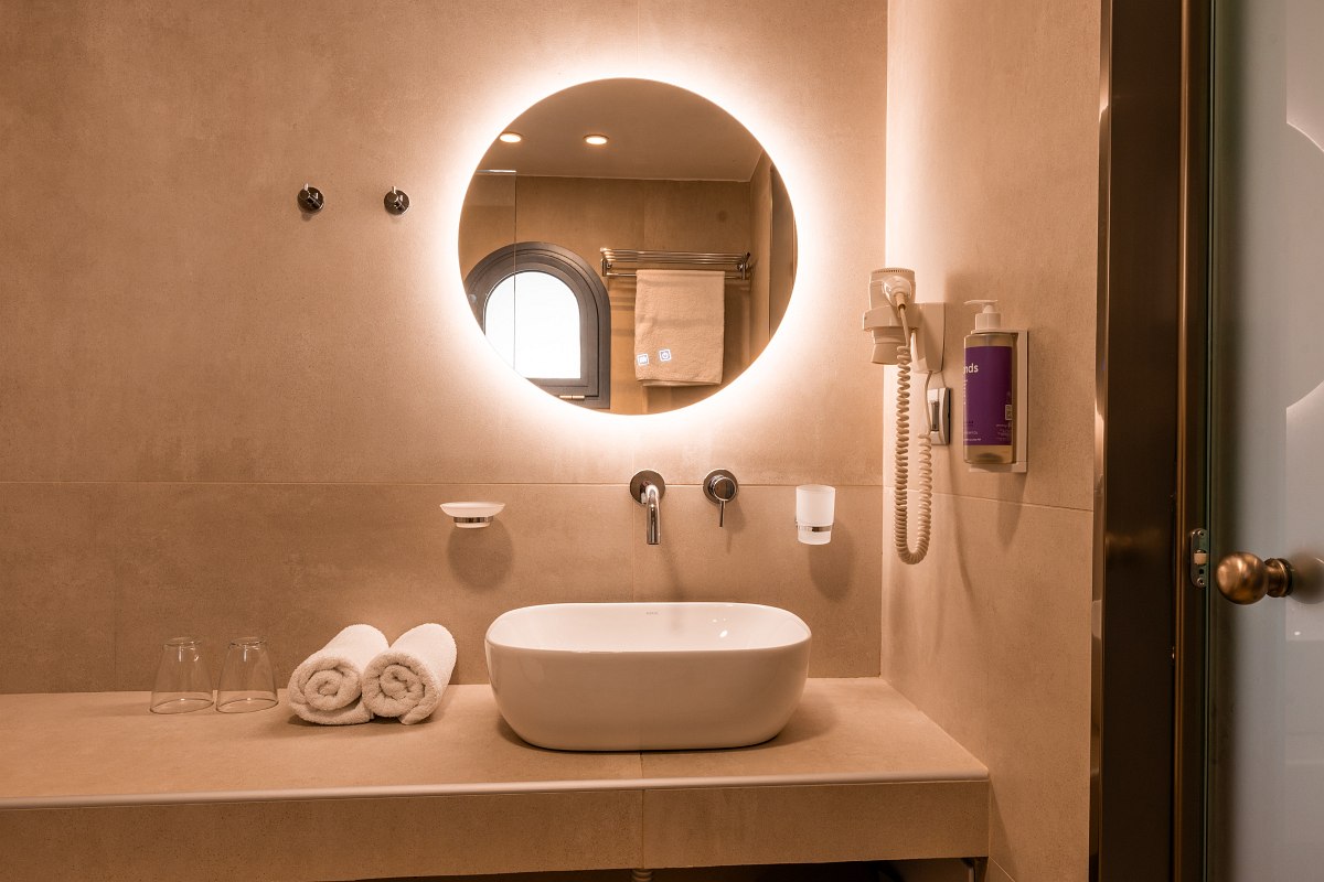 Modernes Badezimmer mit großem runden Spiegel, Aufsatzwaschbecken, Handtüchern, Föhn und stilvollem Lichtkonzept.
