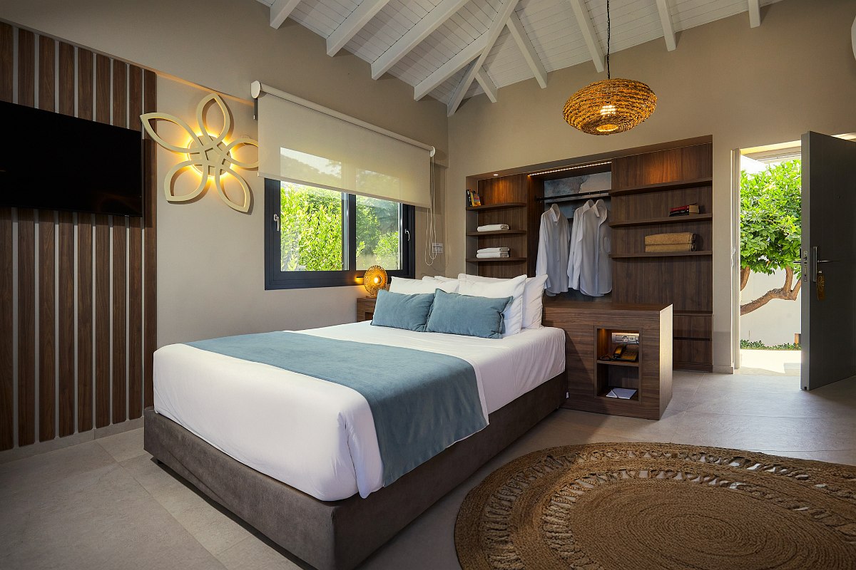 Helles Hotelzimmer mit gemütlichem Doppelbett, offenen Holzregalen, modernem Badbereich und freigelegten Dachbalken.