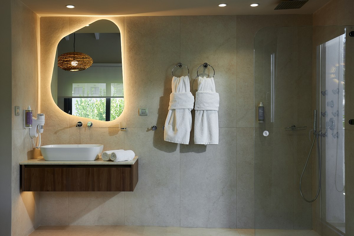 Helles, modernes Hotelzimmer mit Doppelbett, offenem Kleiderschrank, Holzdetails und integriertem Badbereich.
