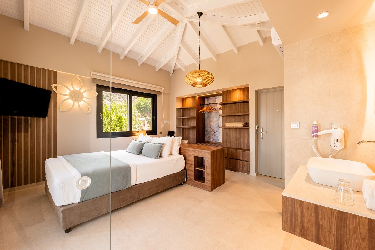 Helles, modernes Hotelzimmer mit Doppelbett, offenem Kleiderschrank, Holzdetails und integriertem Badbereich.