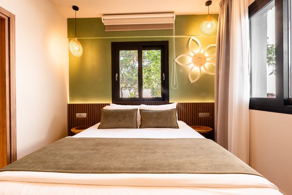 Modernes Hotelzimmer mit gemütlichem Doppelbett, grünem Akzent an der Wand, dekorativer Leuchte und großem Fenster.