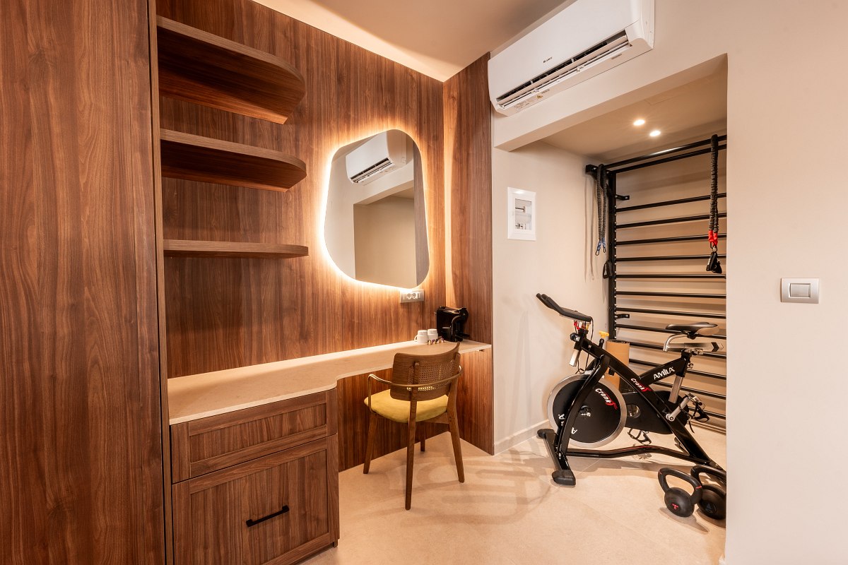 Kompakter Fitnessbereich im Hotelzimmer mit Ergometer, Sprossenwand, Holzschreibtisch und Spiegel mit Beleuchtung.