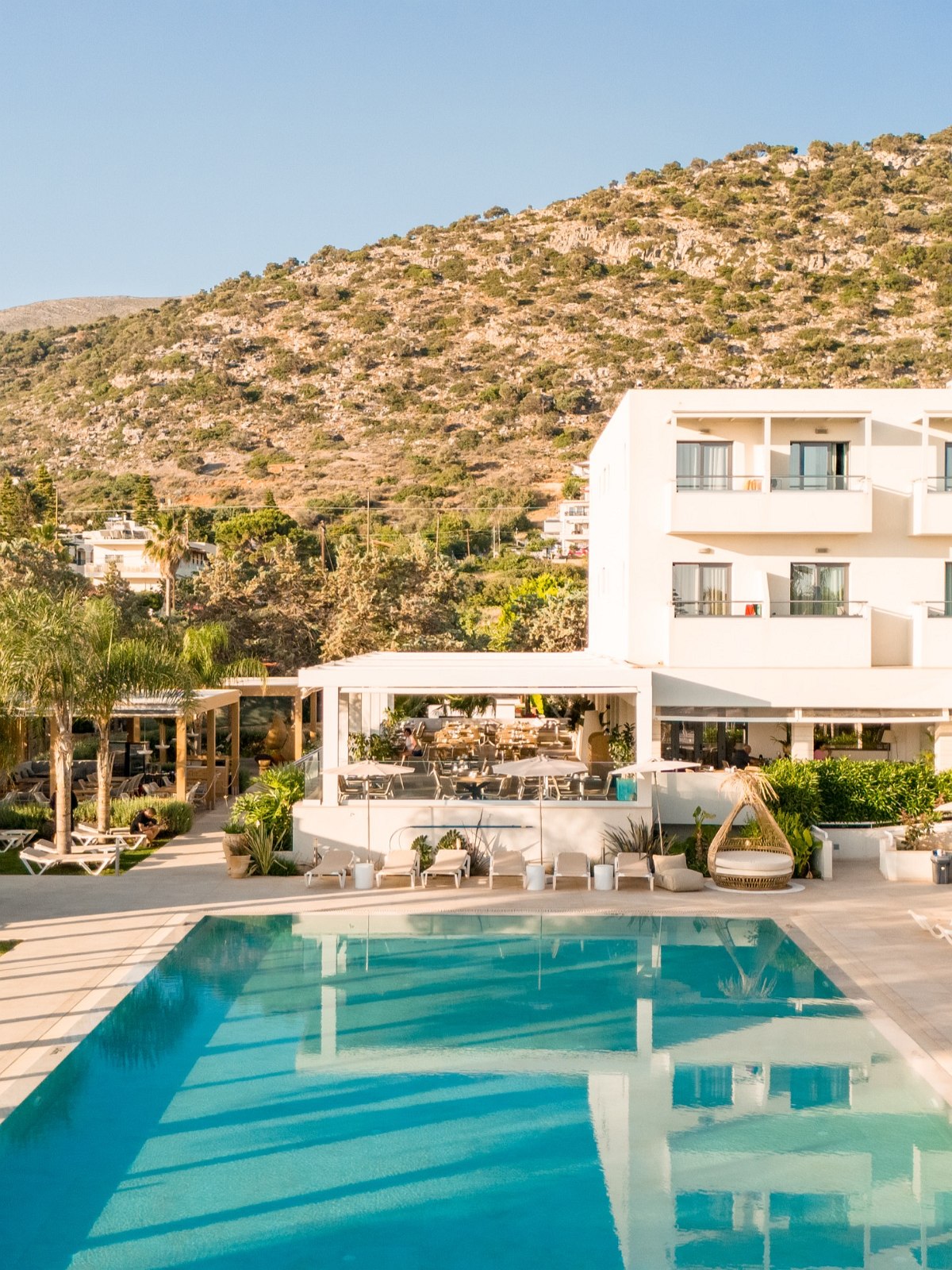 Elegant gedeckter Tisch im Außenbereich eines Restaurants mit Blick auf Palmen, Pool und Lounge-Bereich im Hintergrund.