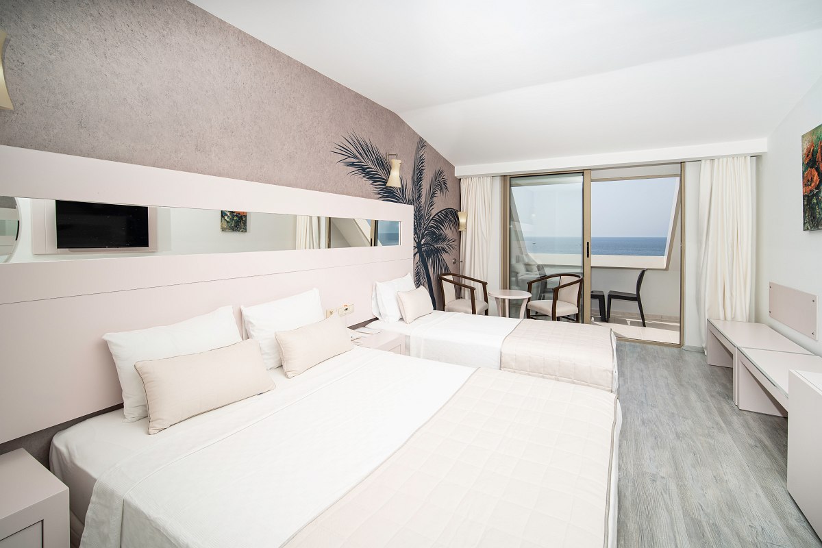 Modernes Hotelzimmer mit zwei Betten, Sitzbereich und Balkon mit Meerblick bei hellem Tageslicht.