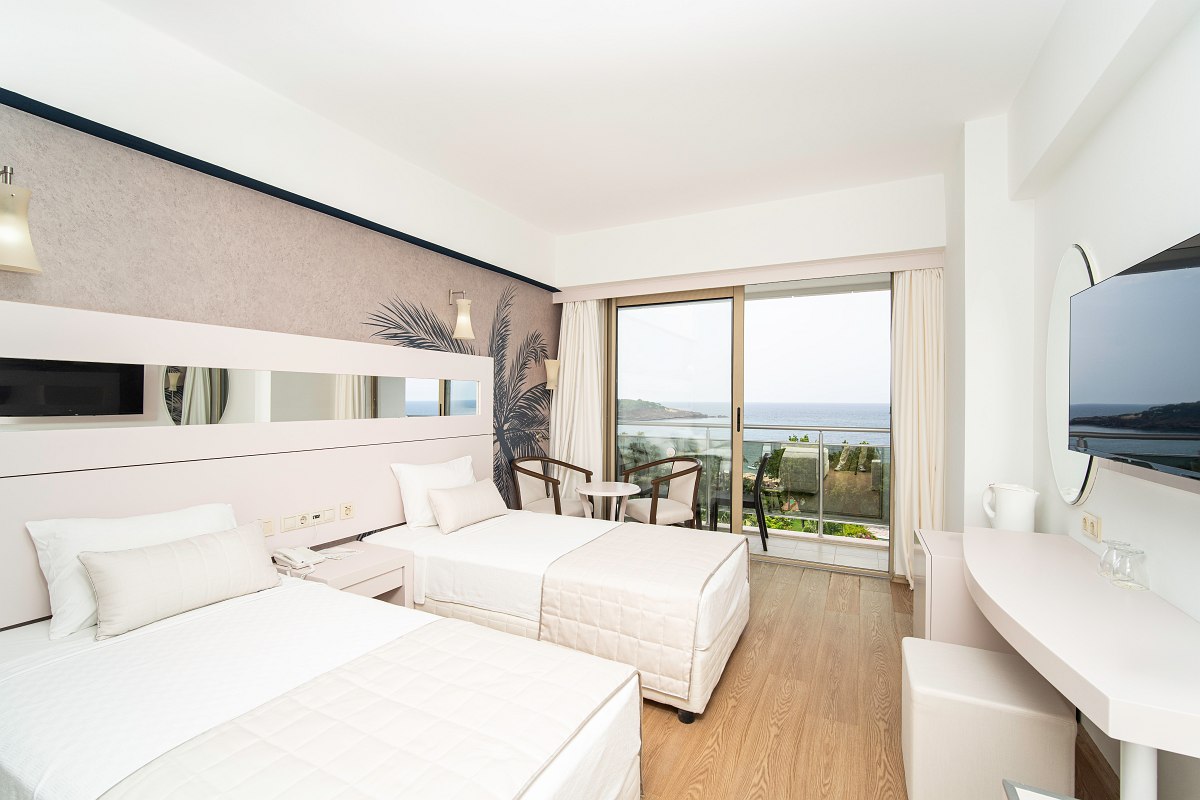 Modernes Hotelzimmer mit zwei Einzelbetten, Sitzbereich und Balkon mit Meerblick bei Tageslicht. 2/2