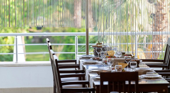 Elegant gedeckter Restauranttisch mit Glasvorhang und Blick ins Grüne auf Garten und Palmen.