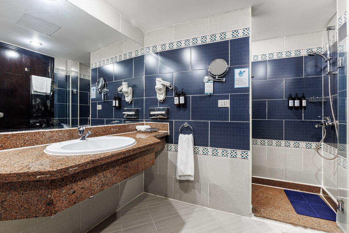 Helles Hotelzimmer mit Doppelbett, türkisfarbenen Akzenten, Fliesenboden und Zugang zur Terrasse durch eine Glastür.