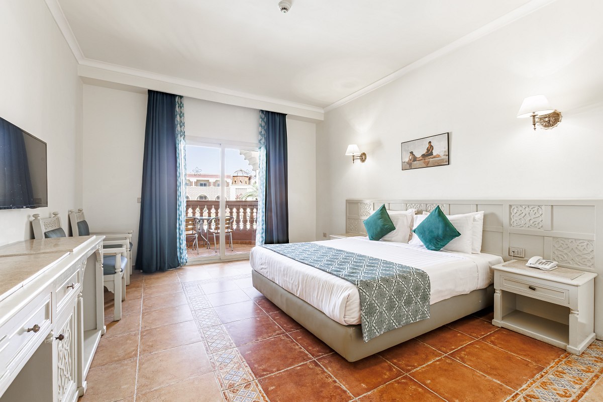 Hotelzimmer mit Doppelbett, orientalisch gestaltetem Schminktisch, Fliesenboden und Zugang zur Terrasse mit Gartenblick.