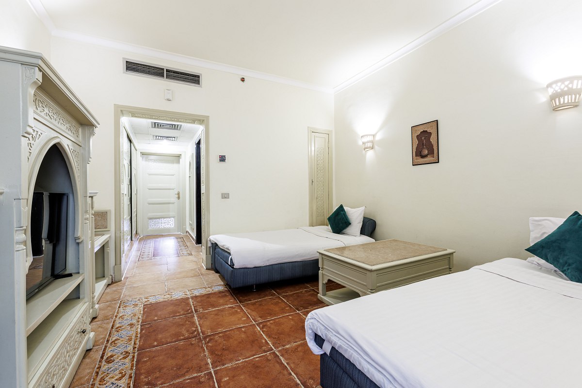 Hotelzimmer mit Doppelbett, orientalisch gestaltetem Schminktisch, Fliesenboden und Zugang zur Terrasse mit Gartenblick.