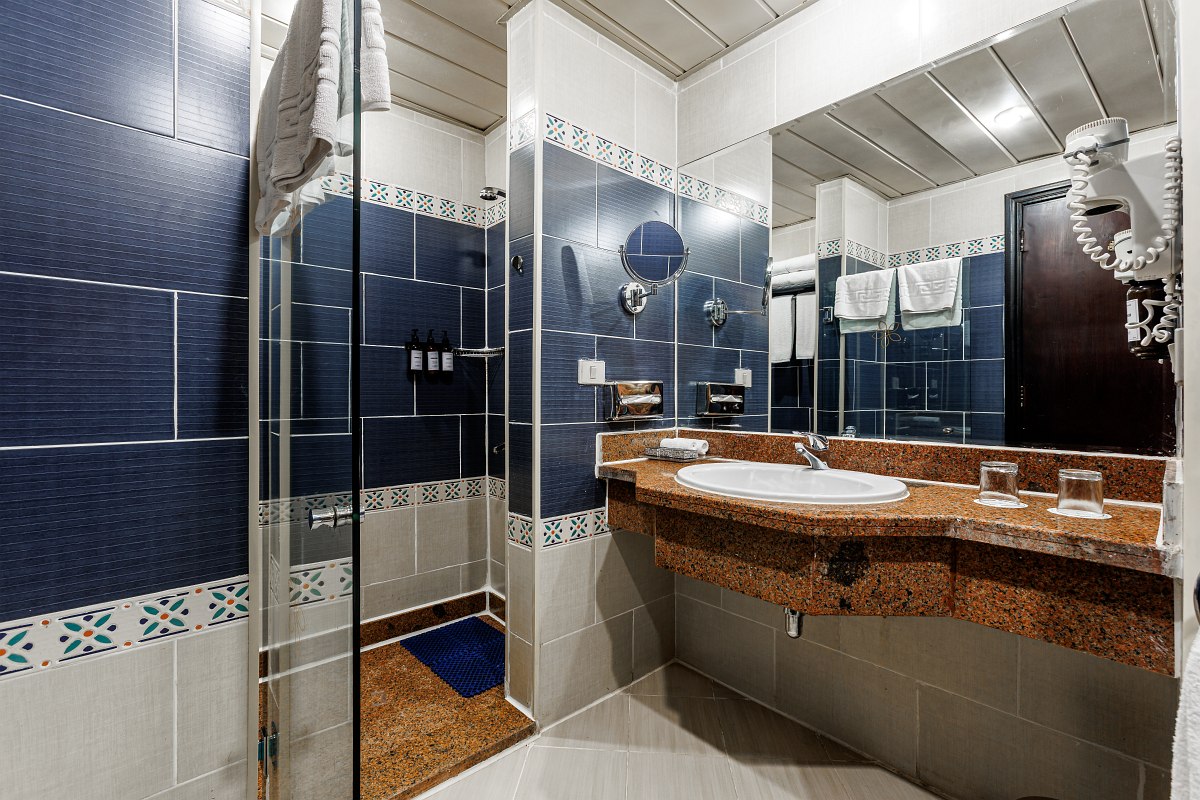 Hotelzimmer mit Doppelbett, orientalisch gestaltetem Schminktisch, Fliesenboden und Zugang zur Terrasse mit Gartenblick.