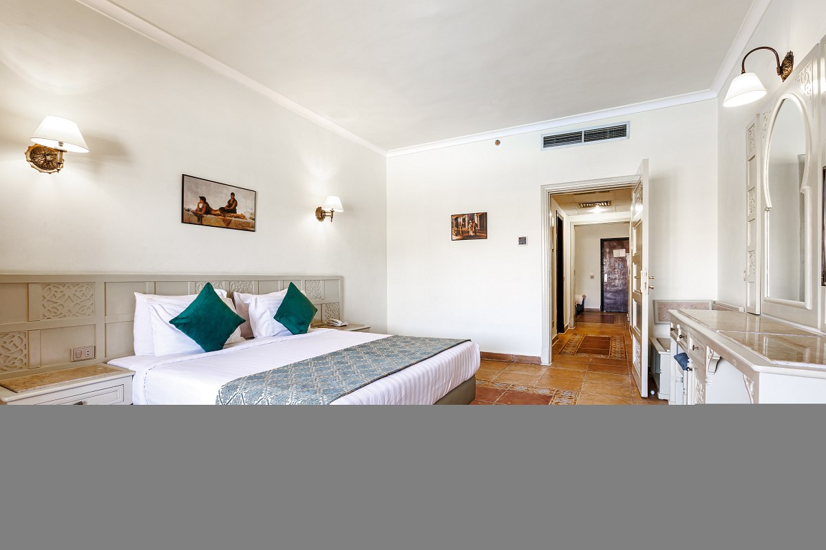 Balkon mit Glas-Tisch und Stühlen, eingerahmt von einem orientalischen Bogen, mit Blick auf Garten und Hotelanlage.