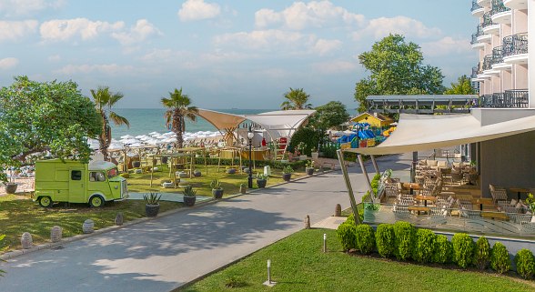Blick von der Hotelterrasse auf den Strand und die Strandbar, Tische mit gemütlichen Stühlen.