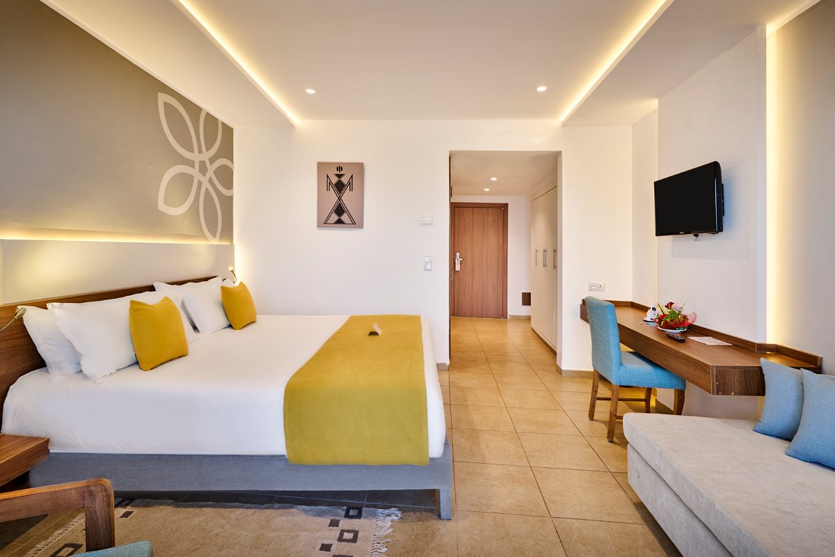 Modernes Hotelzimmer mit großem Bett, gemütlicher Couch, dekorativen Hängeleuchten und Pflanzen.