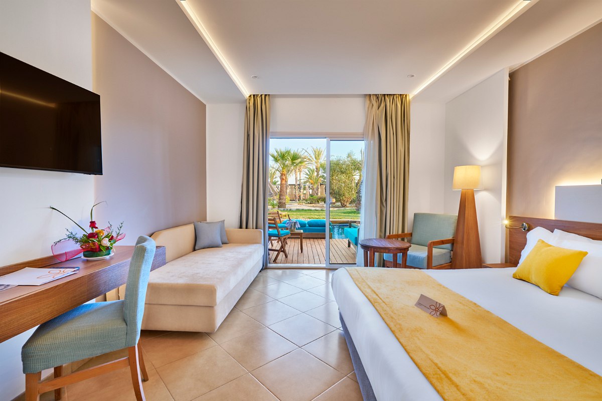 Modernes Hotelzimmer mit großem Doppelbett, hellem Marmorboden, Sitzbereich und Zugang zu privatem Pool im Garten.