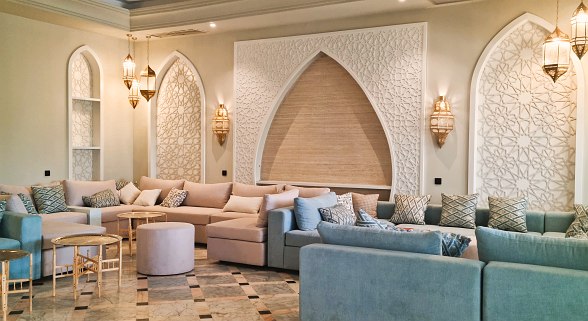 Modernes Hotellobby mit hellen Marmorböden, stilvollen Sofas und dekorativer Trennwand im arabischen Design.