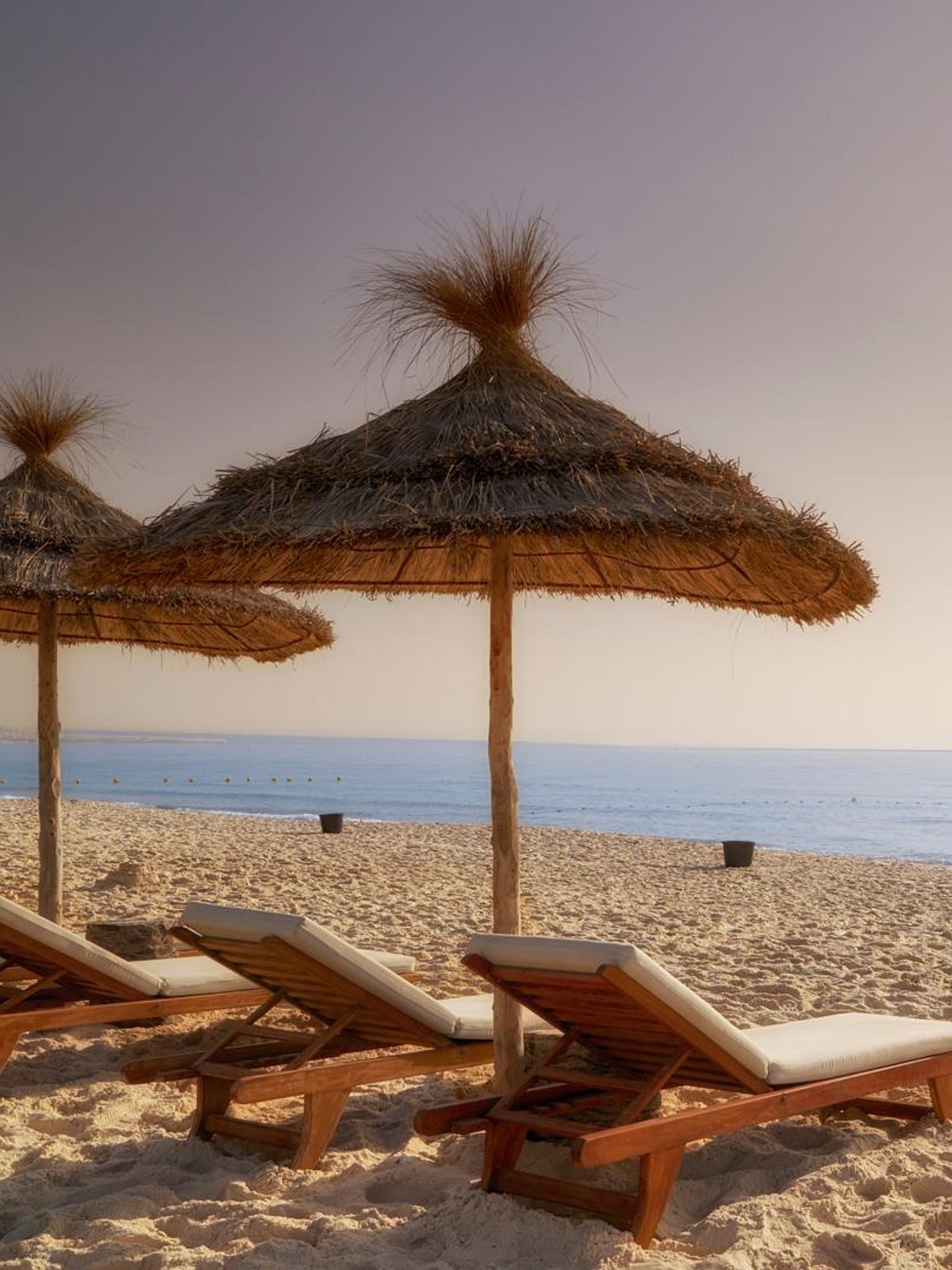 Luftaufnahme eines Hotels mit großem Pool, Strandliegen und Sonnenschirmen direkt am klaren Meer, umgeben von grüner Landschaft.