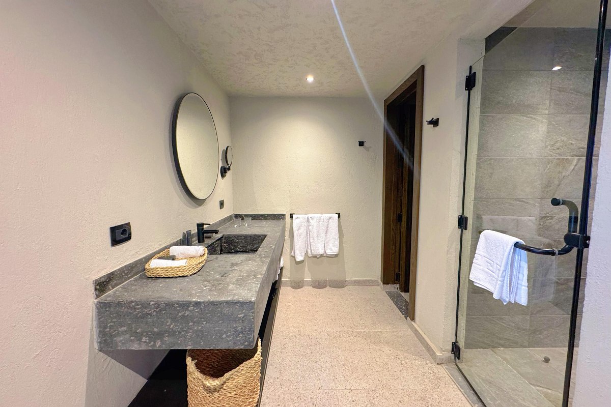 „Modernes Hotelbad mit großer Glasdusche, Steinwaschtisch, rundem Spiegel und hellen Wänden.“