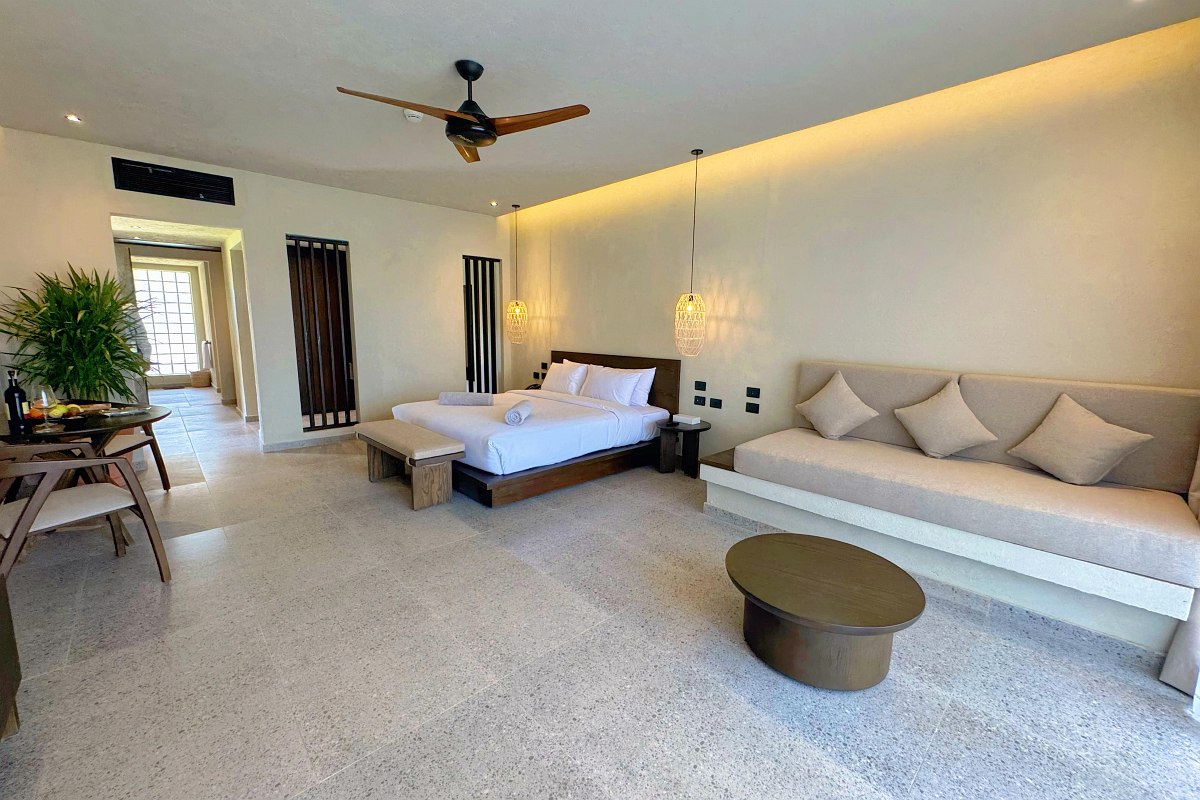 Geräumiges, modernes Hotelzimmer mit Doppelbett, Sofa, Deckenventilator und hellem, minimalistischem Design.“