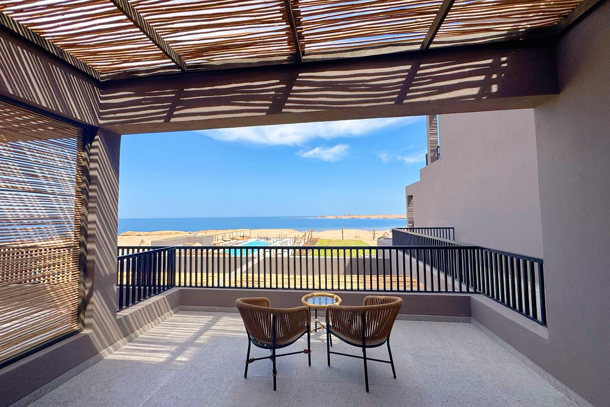 „Überdachte Terrasse mit zwei Stühlen, Tisch und Meerblick unter einem modernen Sonnenschutz aus Holzlamellen.“