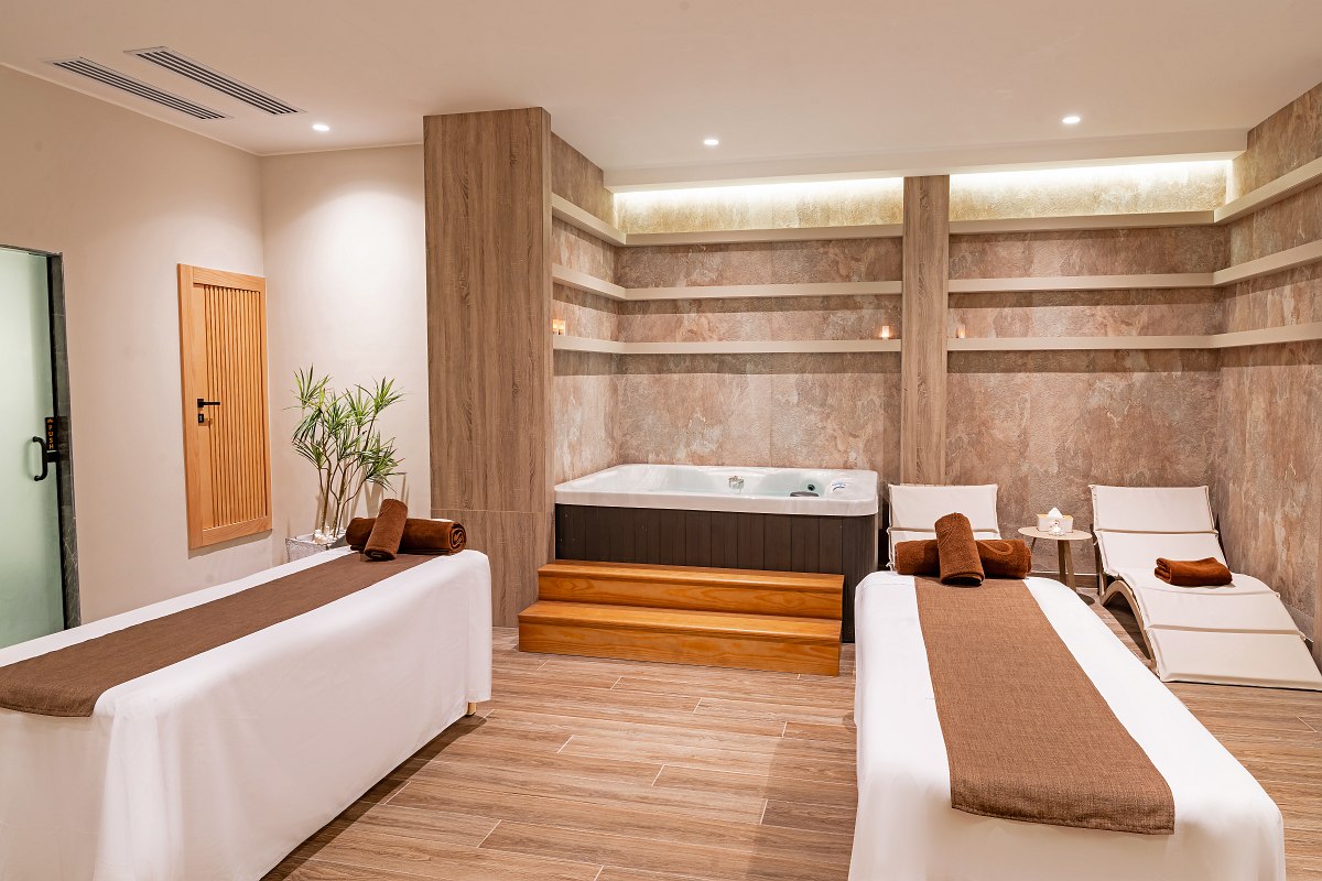 „Moderner Spa-Raum mit zwei Massageliegen, Whirlpool, Liegestühlen und entspannender Beleuchtung.“